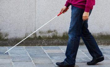 Persona cieca (di cui si vedono solo gambe e busto) cammina per strada con bastone bianco