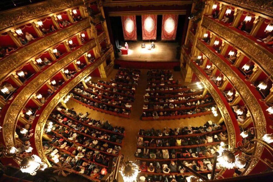 Veduta dall'alto del Teatro Carignano di Torino, durante una rappresentazione teatrale. Platea e palchi con pubblico, palcoscenico con sipario aperto e attori. 